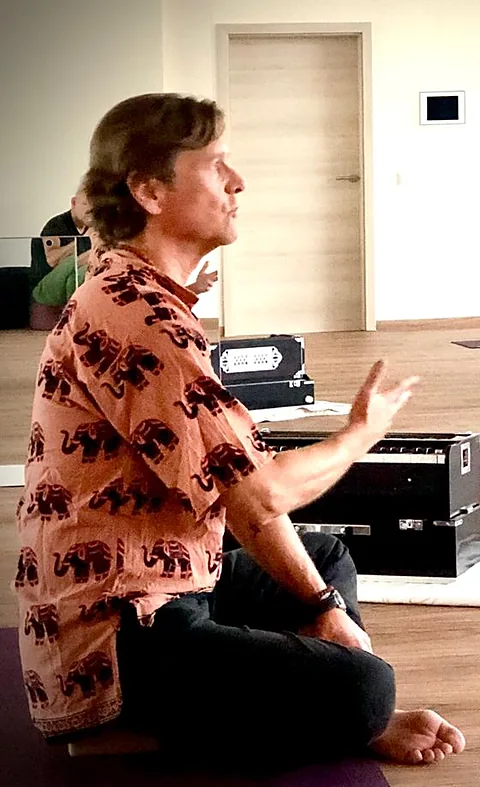 Werner Hauschild sitzt im Schneidersitz vor seinem Harmonium, eine Hand erhoben